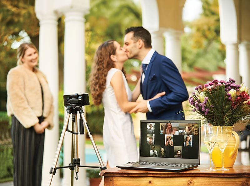 Smart phone on a tripod live streaming a young bride and groom's wedding ceremony for online guests outside in their backyard at home